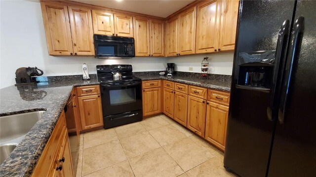 kitchen with dark stone countertops, sink, light tile patterned floors, and black appliances