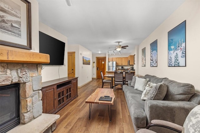 living room with a stone fireplace, ceiling fan, and light hardwood / wood-style floors