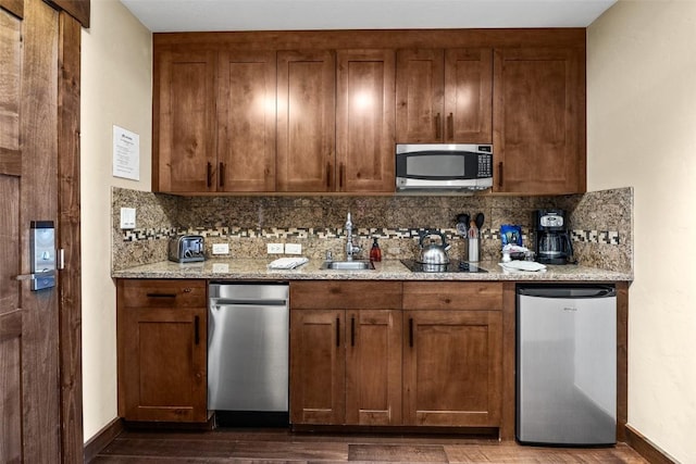 kitchen featuring light stone countertops, dark wood-type flooring, black electric stovetop, sink, and fridge