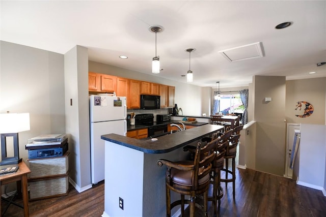 kitchen featuring dark wood-type flooring, kitchen peninsula, pendant lighting, a breakfast bar, and black appliances