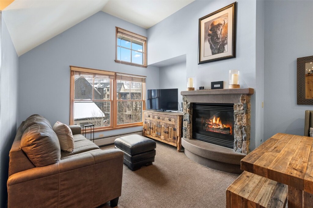 carpeted living room featuring a baseboard radiator, vaulted ceiling, and a fireplace