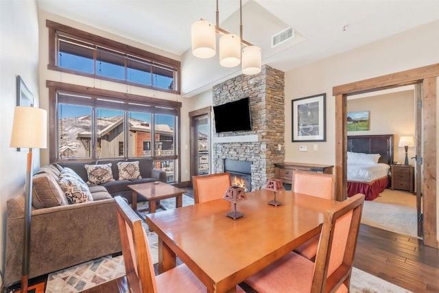 dining area with hardwood / wood-style flooring, a stone fireplace, and a towering ceiling