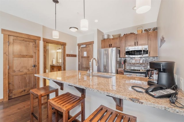 kitchen featuring sink, appliances with stainless steel finishes, hanging light fixtures, dark hardwood / wood-style floors, and light stone counters