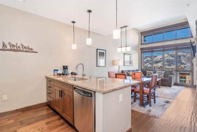 kitchen with sink, hanging light fixtures, stainless steel dishwasher, kitchen peninsula, and light stone countertops