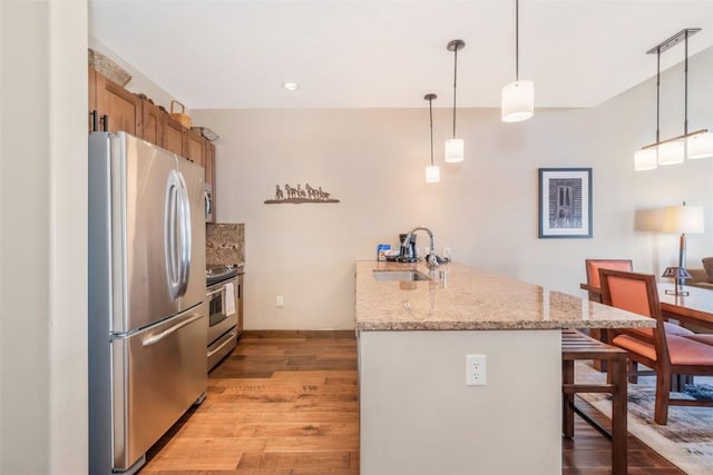 kitchen with sink, a kitchen bar, hanging light fixtures, light stone counters, and stainless steel appliances