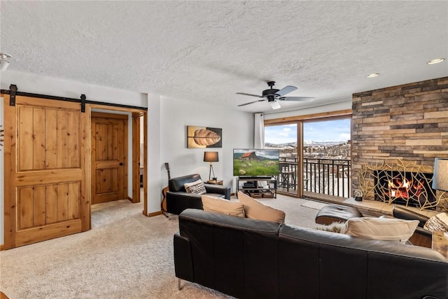 living room with a barn door, a stone fireplace, carpet floors, and a textured ceiling