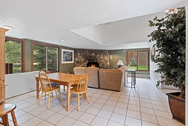 dining area with a stone fireplace, light tile patterned flooring, and a textured ceiling