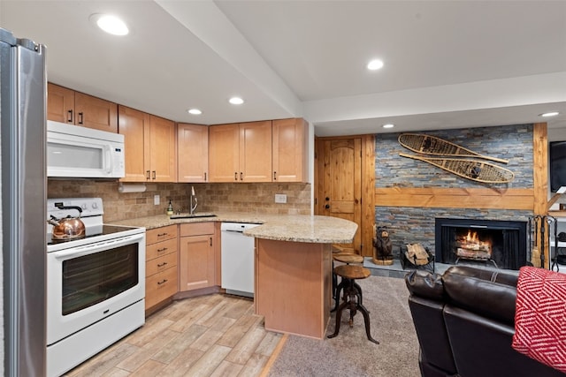 kitchen with white appliances, sink, a fireplace, light hardwood / wood-style floors, and a kitchen bar