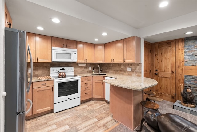 kitchen featuring a breakfast bar, white appliances, light stone countertops, tasteful backsplash, and kitchen peninsula