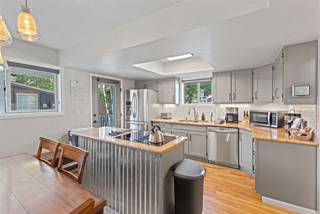 kitchen with tasteful backsplash, stainless steel appliances, sink, pendant lighting, and light hardwood / wood-style flooring