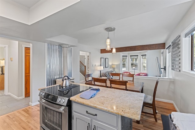 kitchen with hanging light fixtures, electric range, a kitchen island, light hardwood / wood-style floors, and light stone counters