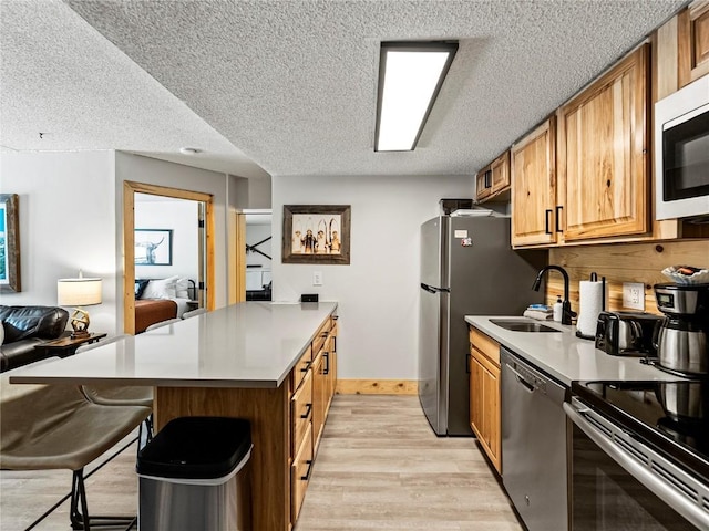 kitchen with appliances with stainless steel finishes, a kitchen breakfast bar, a textured ceiling, sink, and light hardwood / wood-style flooring