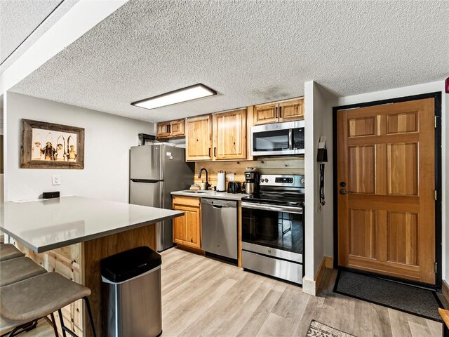 kitchen with sink, light hardwood / wood-style flooring, appliances with stainless steel finishes, a kitchen bar, and kitchen peninsula