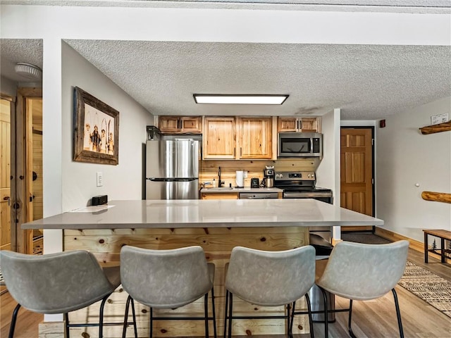 kitchen with a kitchen breakfast bar, a textured ceiling, stainless steel appliances, and light hardwood / wood-style flooring