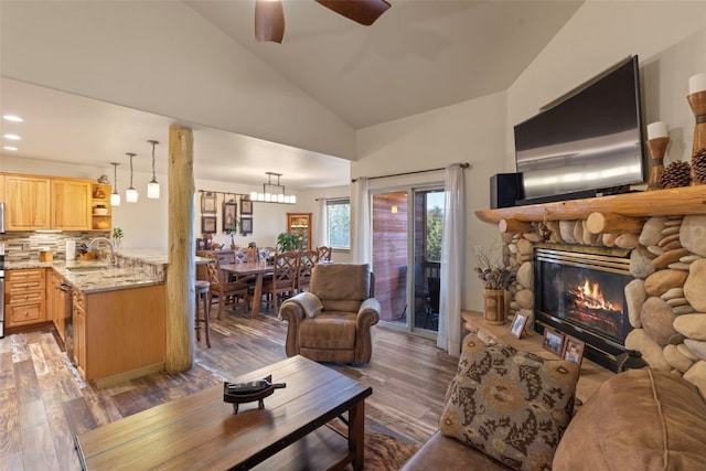 living room with ceiling fan, sink, dark wood-type flooring, a stone fireplace, and vaulted ceiling