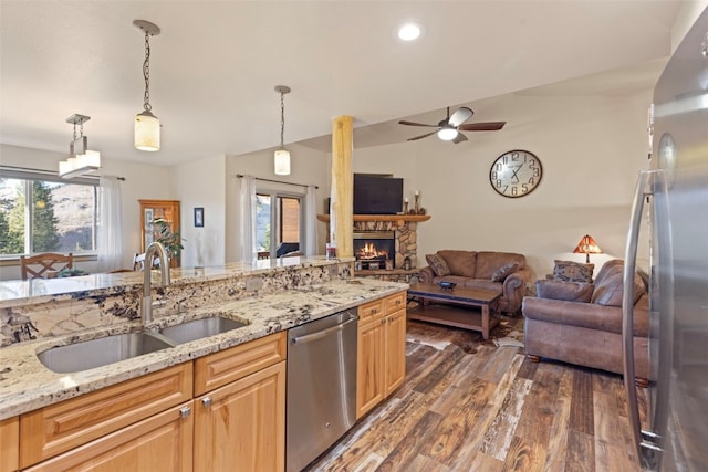 kitchen with light stone countertops, appliances with stainless steel finishes, ceiling fan, sink, and a fireplace