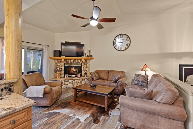 living room featuring dark wood-type flooring, vaulted ceiling, ceiling fan, and a stone fireplace