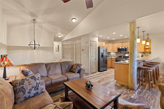 living room with ceiling fan with notable chandelier, light hardwood / wood-style flooring, and lofted ceiling