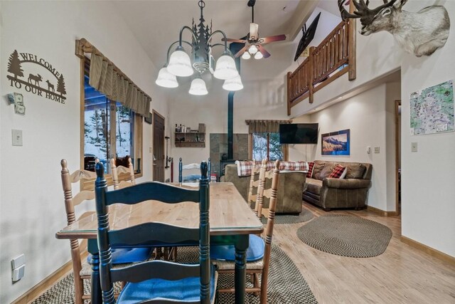 dining space featuring a high ceiling, ceiling fan with notable chandelier, and light hardwood / wood-style flooring