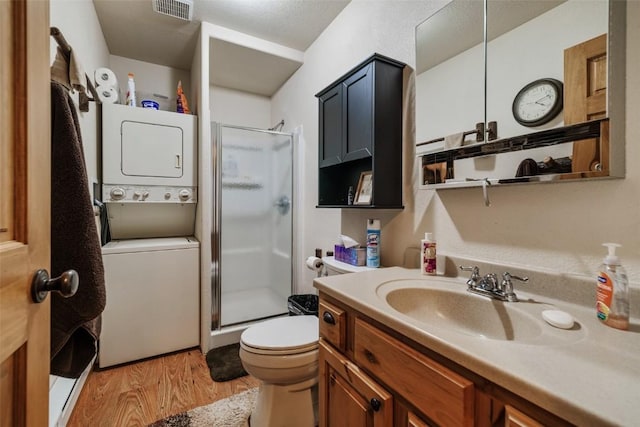 bathroom with stacked washing maching and dryer, vanity, a shower with door, hardwood / wood-style floors, and toilet