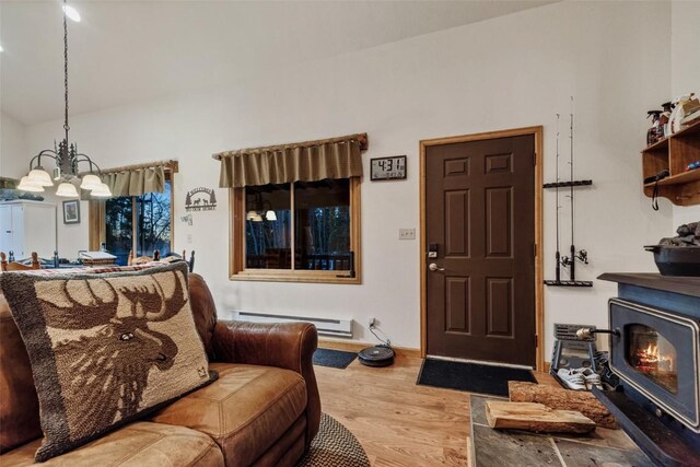 living room featuring a wood stove, a baseboard radiator, a notable chandelier, and light wood-type flooring