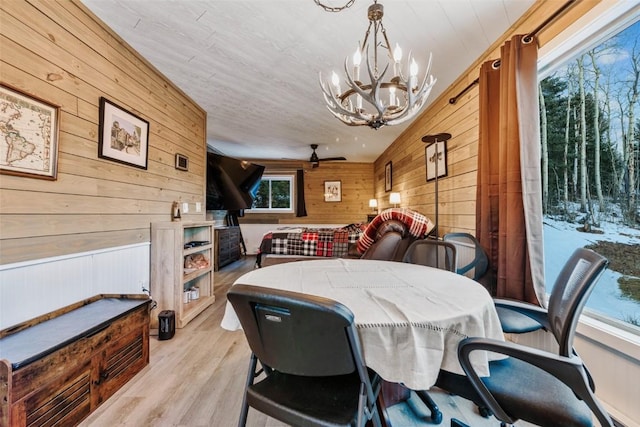 dining area featuring lofted ceiling, ceiling fan with notable chandelier, wooden walls, and a healthy amount of sunlight