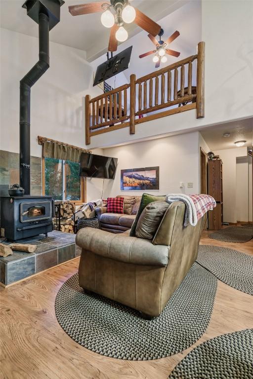 living room with ceiling fan, wood-type flooring, a wood stove, and a high ceiling