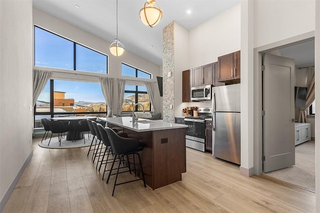 kitchen with a kitchen bar, appliances with stainless steel finishes, pendant lighting, a high ceiling, and an island with sink