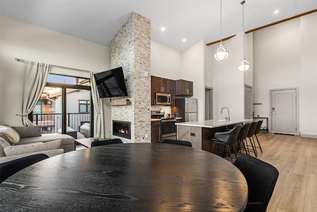 dining room with a stone fireplace, light hardwood / wood-style flooring, high vaulted ceiling, and sink