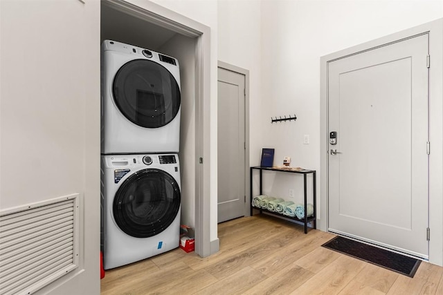 clothes washing area with light hardwood / wood-style flooring and stacked washer / drying machine