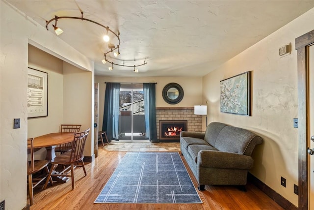 sitting room featuring baseboards, a brick fireplace, wood finished floors, and rail lighting