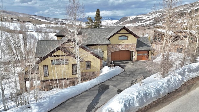 view of front of house with driveway, roof with shingles, a garage, stone siding, and a mountain view