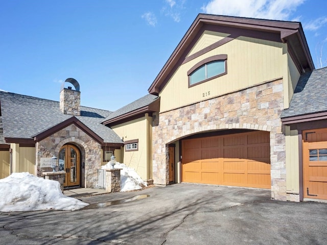 view of front of property with stone siding, driveway, a chimney, and a shingled roof