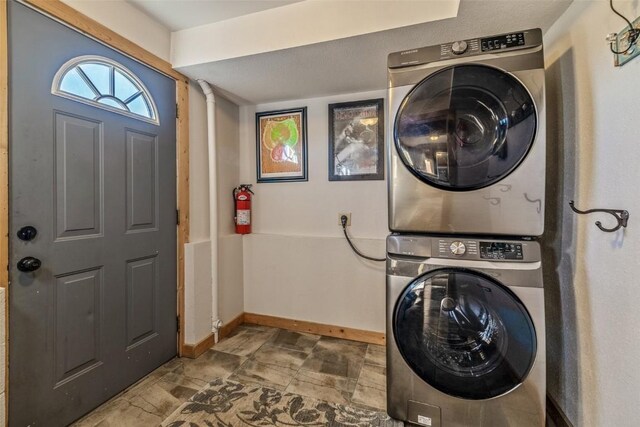 clothes washing area with laundry area, stone finish flooring, baseboards, and stacked washing maching and dryer