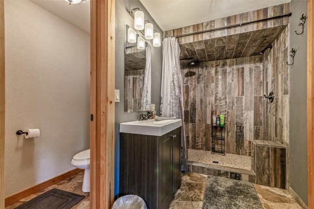 full bathroom with tiled shower, toilet, vanity, and stone finish floor