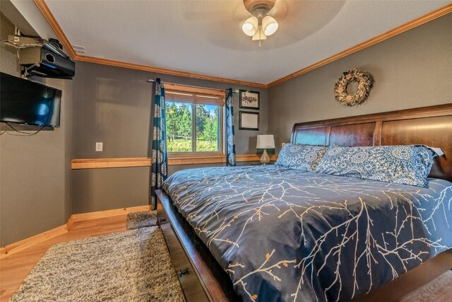 bedroom with baseboards, wood finished floors, ornamental molding, and a ceiling fan