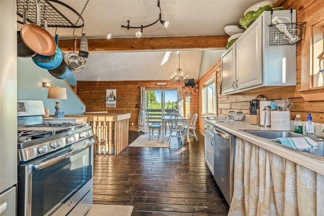 kitchen with an inviting chandelier, dark wood-type flooring, wood walls, appliances with stainless steel finishes, and beamed ceiling