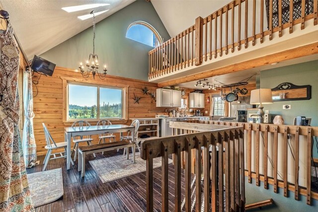 dining room with dark wood-style floors, high vaulted ceiling, a skylight, wood walls, and a chandelier