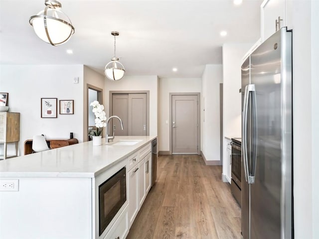 kitchen with white cabinets, sink, an island with sink, decorative light fixtures, and stainless steel appliances