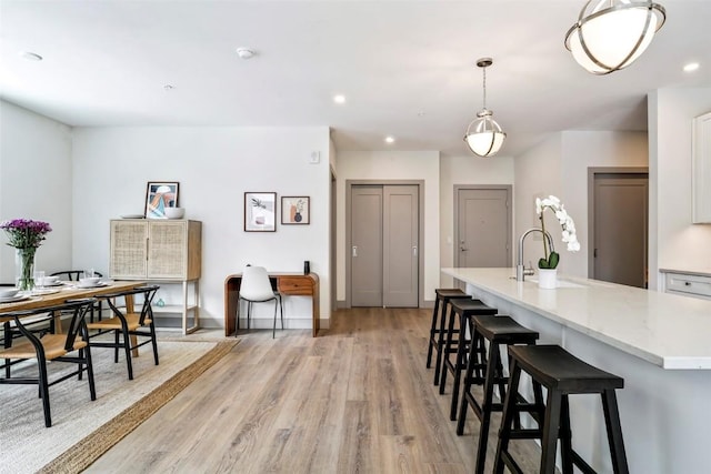 kitchen featuring decorative light fixtures, sink, light wood-type flooring, and an island with sink