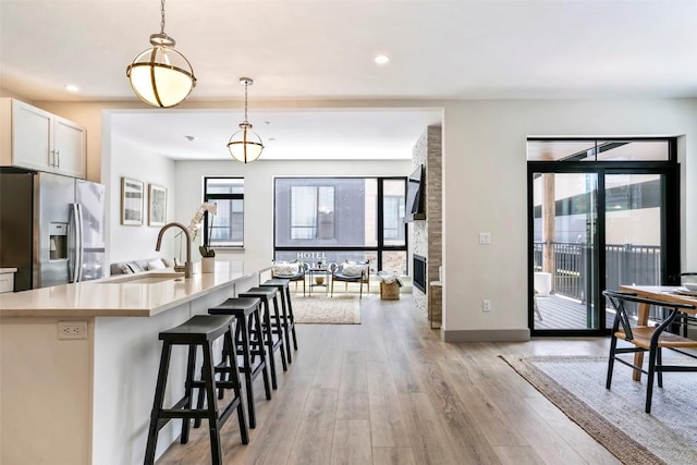 kitchen with white cabinetry, a kitchen breakfast bar, stainless steel refrigerator with ice dispenser, an island with sink, and pendant lighting