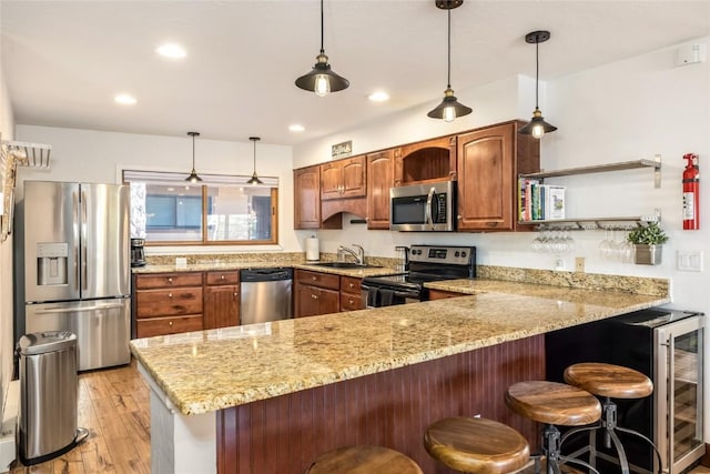 kitchen featuring light stone countertops, light wood-type flooring, a peninsula, stainless steel appliances, and a sink