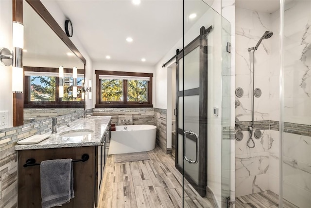 full bath featuring a marble finish shower, a freestanding bath, tile walls, and vanity