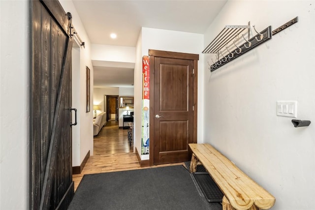 hallway featuring a barn door, baseboards, and light wood-style flooring