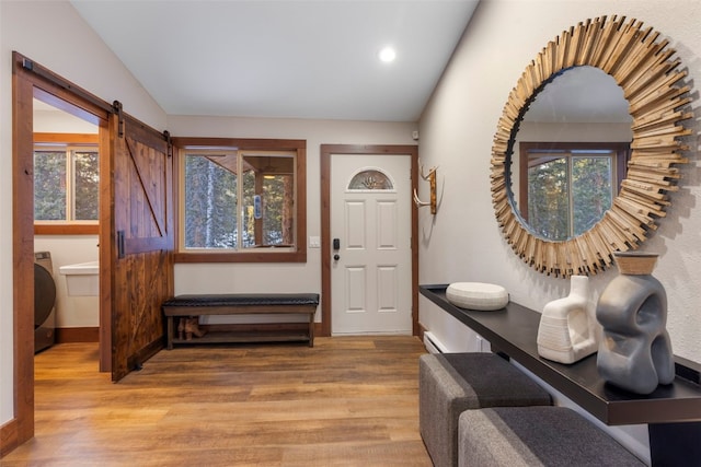 foyer with lofted ceiling, washer / dryer, light hardwood / wood-style floors, and a healthy amount of sunlight