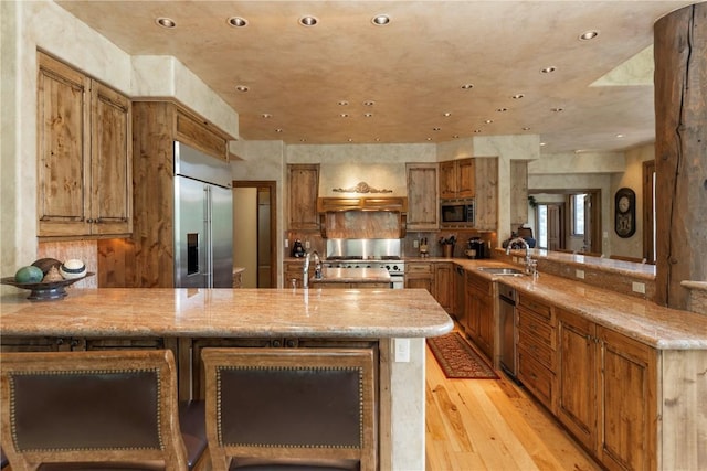 kitchen with a sink, built in appliances, a peninsula, and light wood finished floors