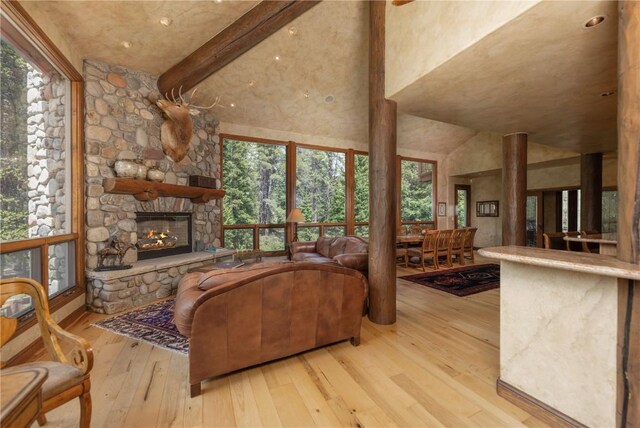 living area featuring beam ceiling, a stone fireplace, a high ceiling, and hardwood / wood-style flooring