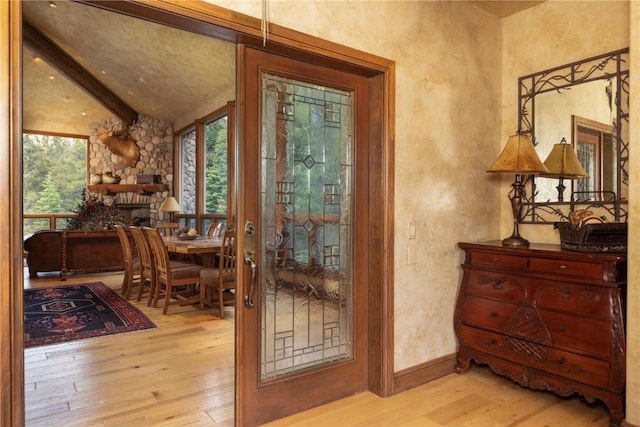 doorway with a wealth of natural light, a stone fireplace, vaulted ceiling with beams, and hardwood / wood-style floors