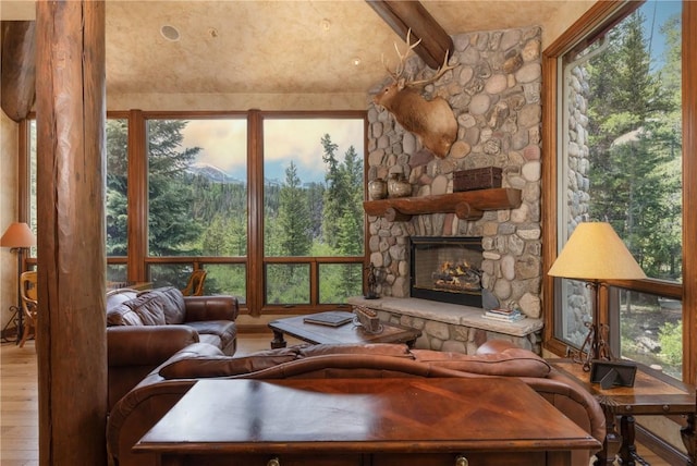 living room featuring a wealth of natural light, beamed ceiling, a stone fireplace, and wood finished floors