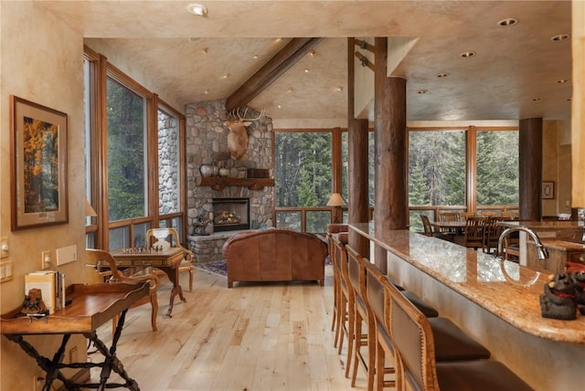 interior space featuring vaulted ceiling with beams, a breakfast bar, a stone fireplace, stone countertops, and wood-type flooring